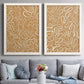 Set of two white barnwood framed canvas prints depicting paired graphic botanical pattern abstracts with leaf-like contours, flat warm backgrounds, and repeated flowing shapes above a sofa in a contemporary living room.