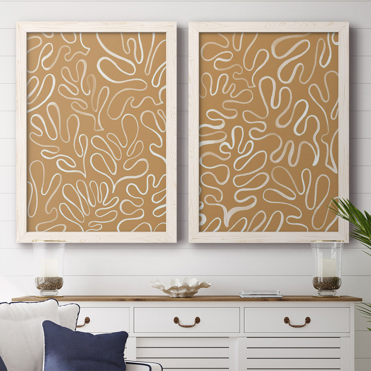 Set of two white barnwood framed canvas prints depicting a coordinated art pair of continuous white organic lines over solid ochre and blush fields rendered as graphic botanical pattern abstracts above a dining room sideboard.