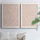 Set of two white barnwood framed canvas prints depicting leaf-like contours, flat warm backgrounds, and repeated flowing shapes arranged across two complementary compositions above a sofa in a bright living space.