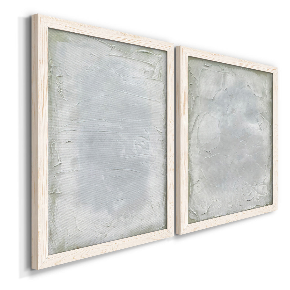 Angled view of a set of two white barnwood framed canvas prints featuring two quiet textural abstracts featuring layered white and silver-gray painted surfaces.