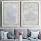 Set of two white barnwood framed canvas prints depicting paired quiet textural abstracts with soft palette-knife marks, cloudy transitions, and nearly monochrome fields above a sofa in a contemporary living room.
