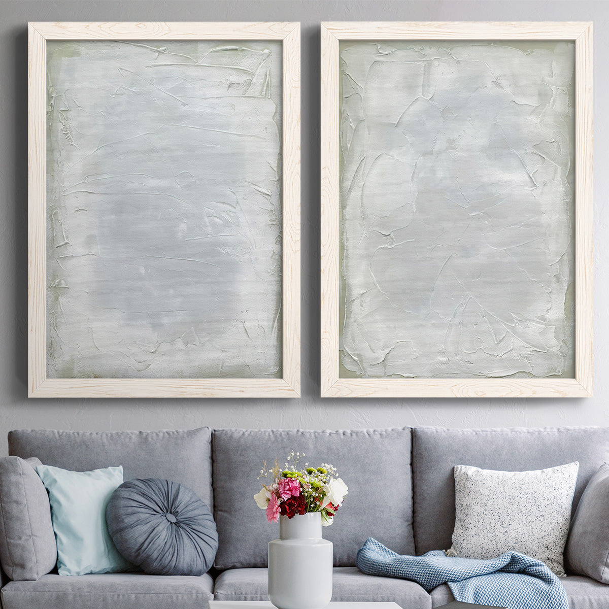 Set of two white barnwood framed canvas prints depicting paired quiet textural abstracts with soft palette-knife marks, cloudy transitions, and nearly monochrome fields above a sofa in a contemporary living room.