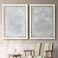 Set of two white barnwood framed canvas prints depicting two quiet textural abstracts featuring layered white and silver-gray painted surfaces above a sideboard in a cozy sitting room.