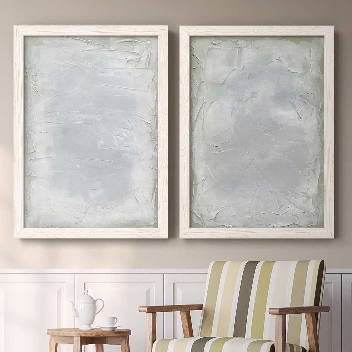 Set of two white barnwood framed canvas prints depicting two quiet textural abstracts featuring layered white and silver-gray painted surfaces above a sideboard in a cozy sitting room.