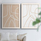 Set of two white barnwood framed canvas prints depicting warm beige grounds, white contour paths, and quiet negative space arranged across two complementary compositions above a sofa in a bright living space.
