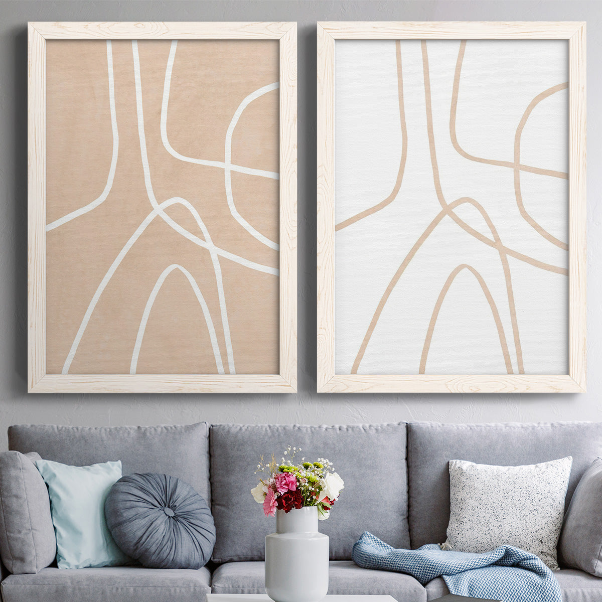 Set of two white barnwood framed canvas prints depicting paired minimalist line abstracts with warm beige grounds, white contour paths, and quiet negative space above a sofa in a contemporary living room.