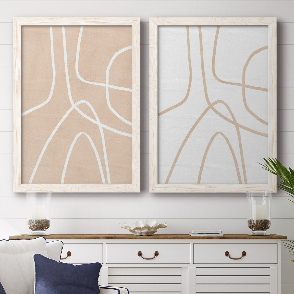 Set of two white barnwood framed canvas prints depicting a coordinated art pair of single continuous tan lines forming oversized organic curves rendered as minimalist line abstracts above a dining room sideboard.