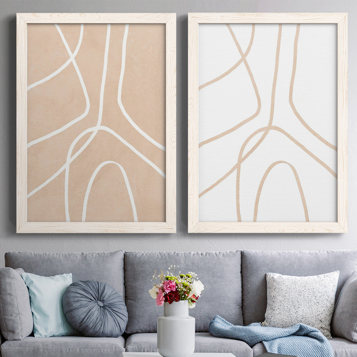 Set of two white barnwood framed canvas prints depicting paired minimalist line abstracts with warm beige grounds, white contour paths, and quiet negative space above a sofa in a contemporary living room.