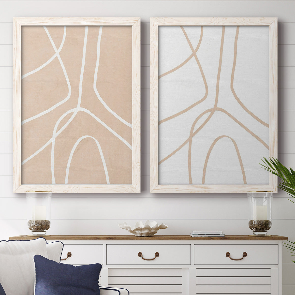 Set of two white barnwood framed canvas prints depicting a coordinated art pair of single continuous tan lines forming oversized organic curves rendered as minimalist line abstracts above a dining room sideboard.