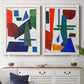 Set of two white barnwood framed canvas prints depicting a coordinated art pair of bold red blue green yellow and black geometric forms rendered as mid-century graphic abstracts above a dining room sideboard.