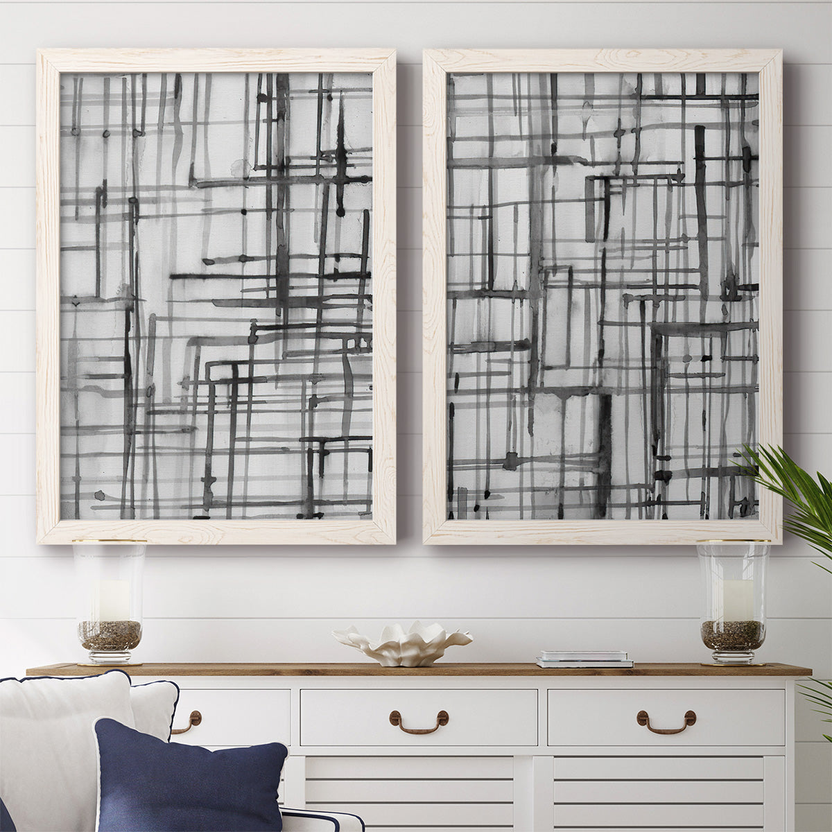 Set of two white barnwood framed canvas prints depicting a coordinated art pair of layered black linear grids rendered as monochrome geometric abstracts above a dining room sideboard.