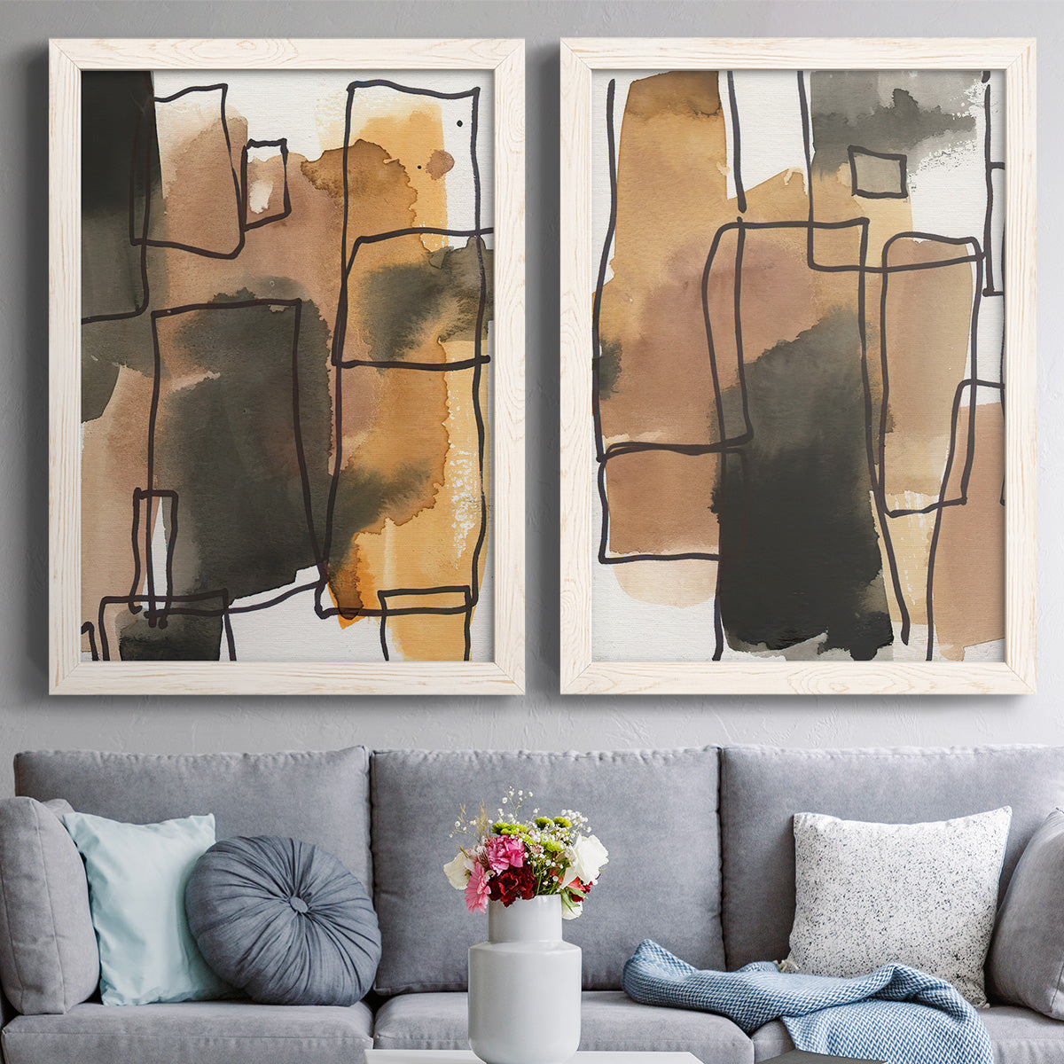 Set of two white barnwood framed canvas prints depicting paired retro geometric abstracts with tan brown gray and cream shapes with loose rectangular structure above a sofa in a contemporary living room.