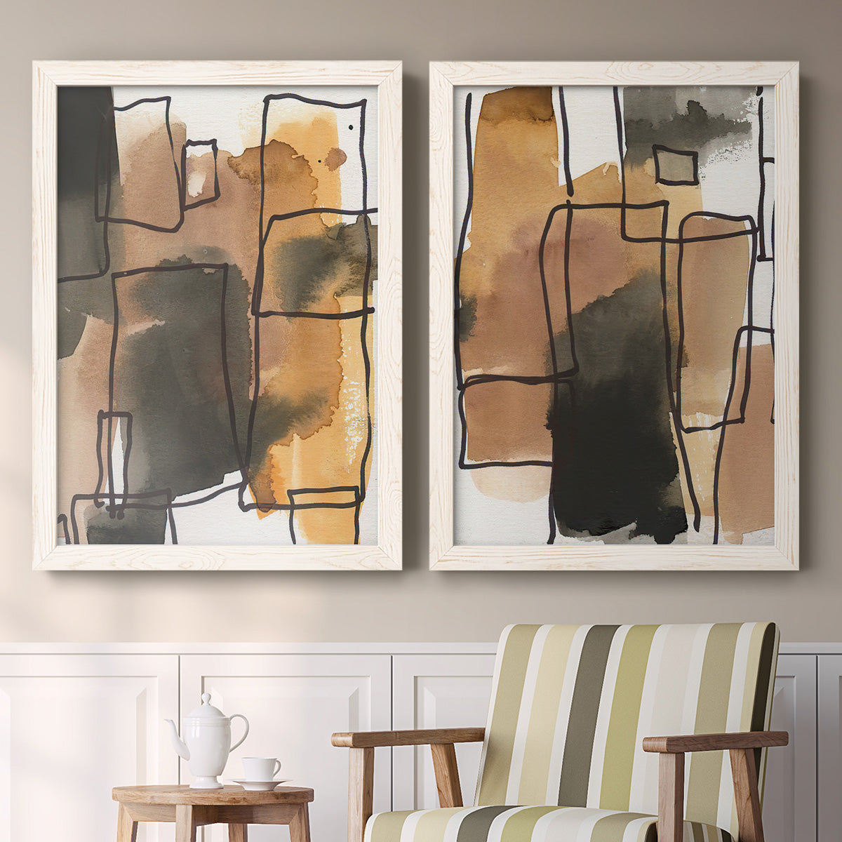 Set of two white barnwood framed canvas prints depicting two retro geometric abstracts featuring earthy watercolor blocks crossed by black contour lines above a sideboard in a cozy sitting room.