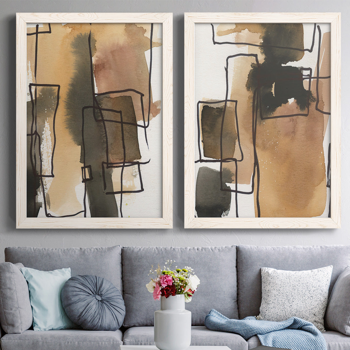Set of two white barnwood framed canvas prints depicting paired retro geometric abstracts with tan brown gray and cream shapes with loose rectangular structure above a sofa in a contemporary living room.