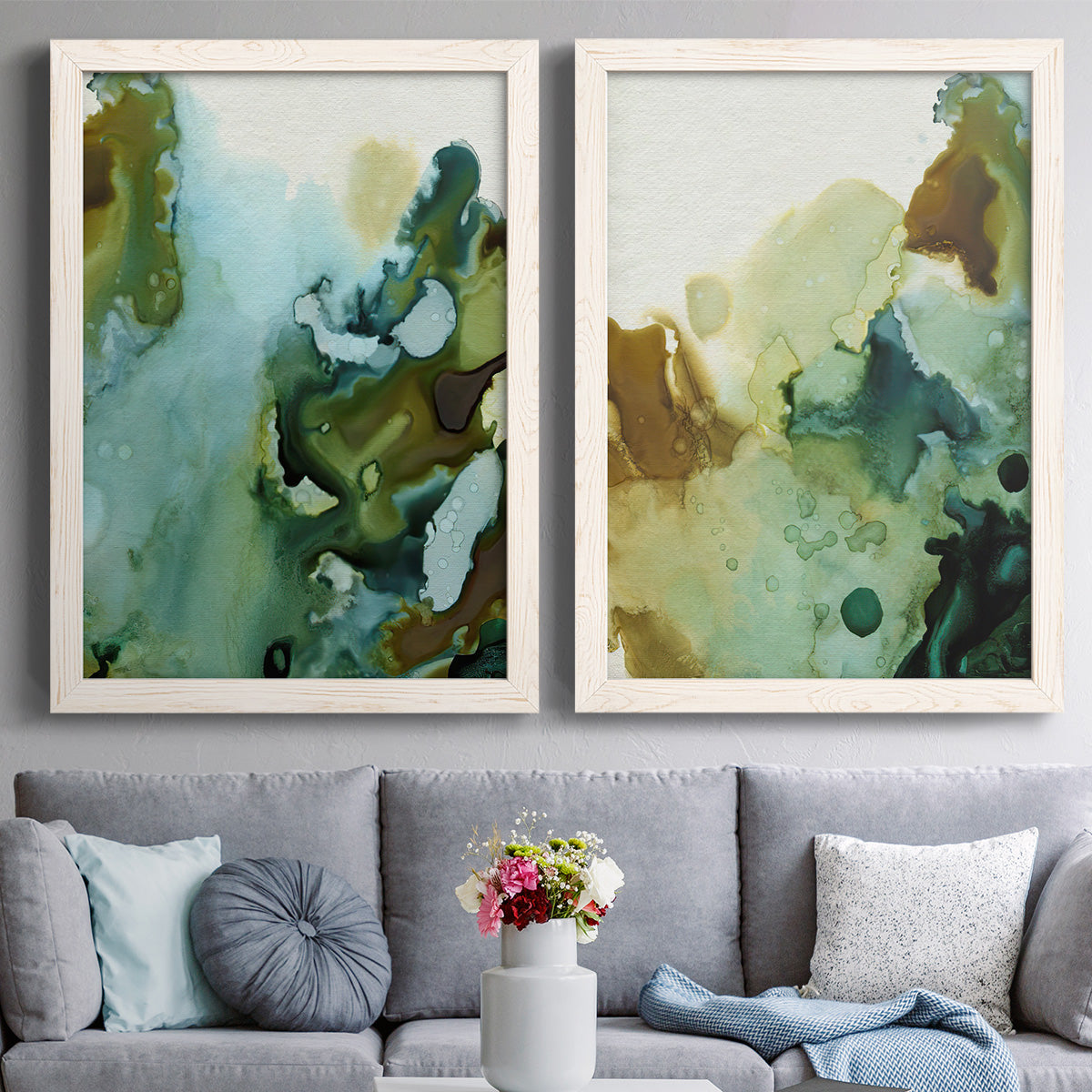 Set of two white barnwood framed canvas prints depicting paired organic watercolor abstracts with translucent washes, dark branching edges, and mineral-like blooms above a sofa in a contemporary living room.