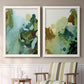 Set of two white barnwood framed canvas prints depicting two organic watercolor abstracts featuring fluid green blue and earthy brown ink pools above a sideboard in a cozy sitting room.