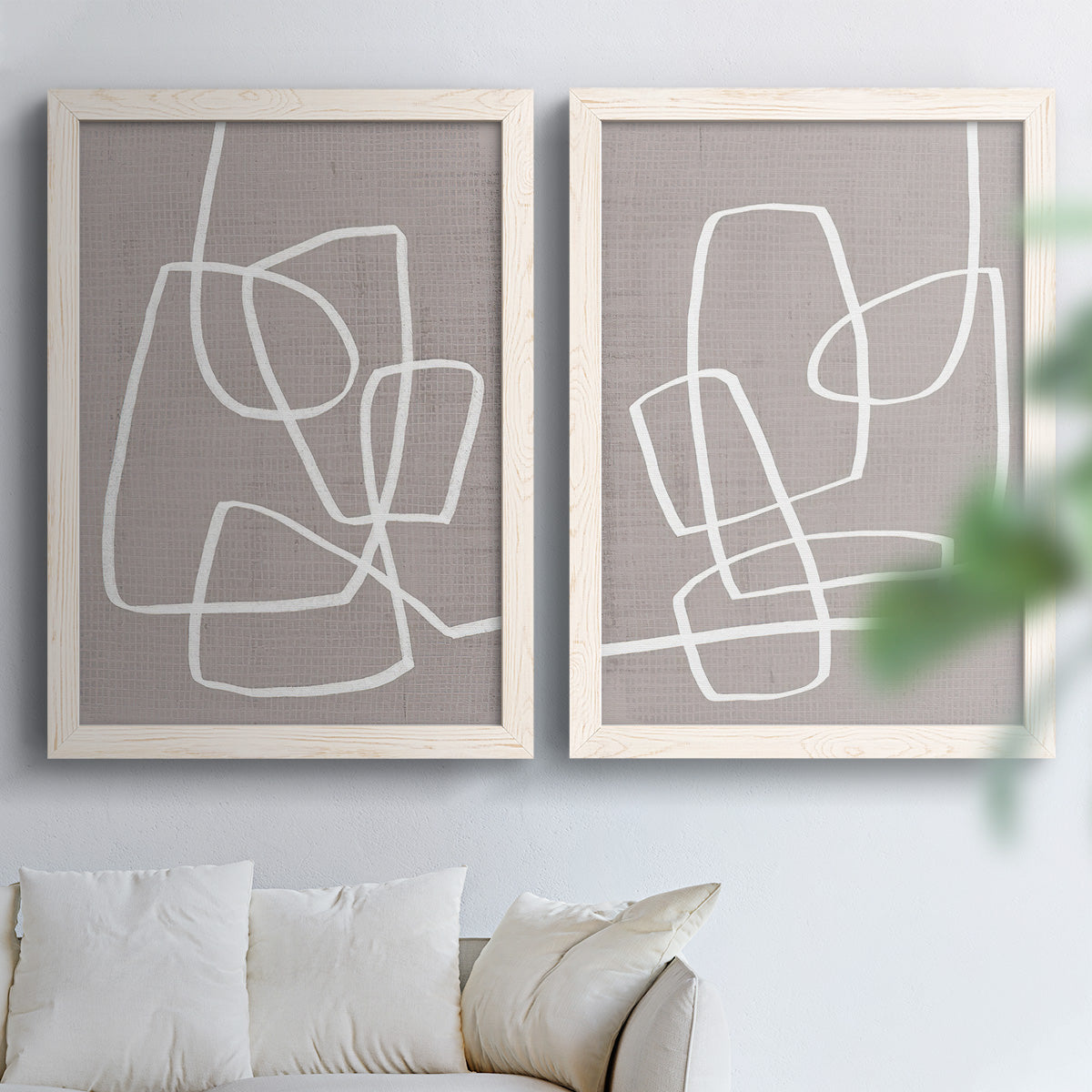 Set of two white barnwood framed canvas prints depicting rounded rectangular contours, soft gray grounds, and sparse composition arranged across two complementary compositions above a sofa in a bright living space.