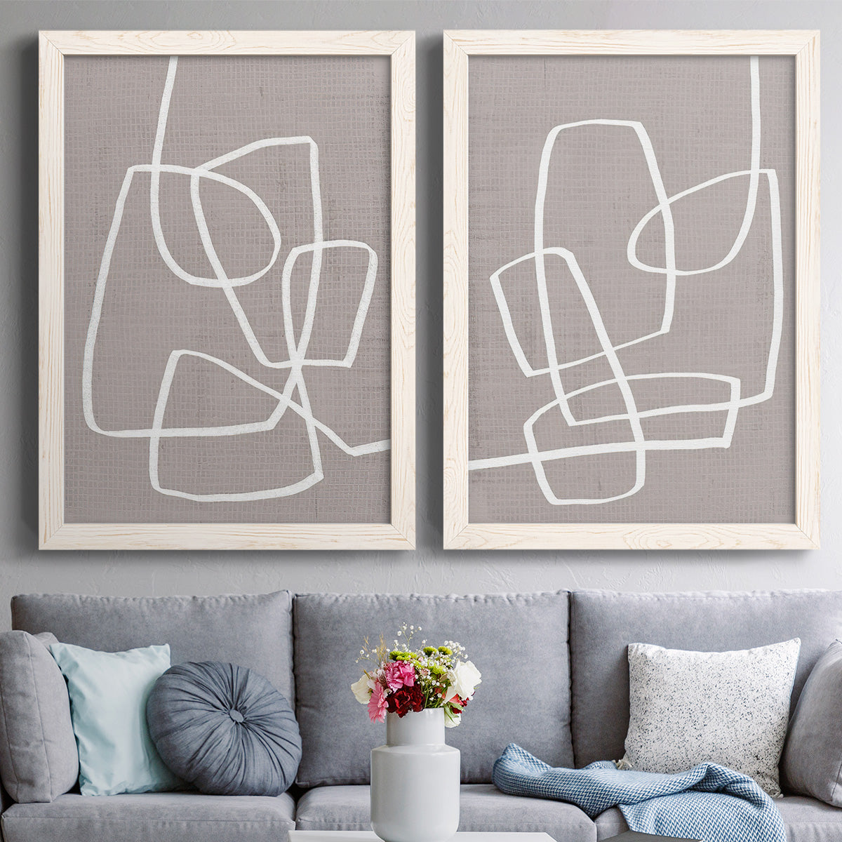 Set of two white barnwood framed canvas prints depicting paired minimalist geometric line art with rounded rectangular contours, soft gray grounds, and sparse composition above a sofa in a contemporary living room.