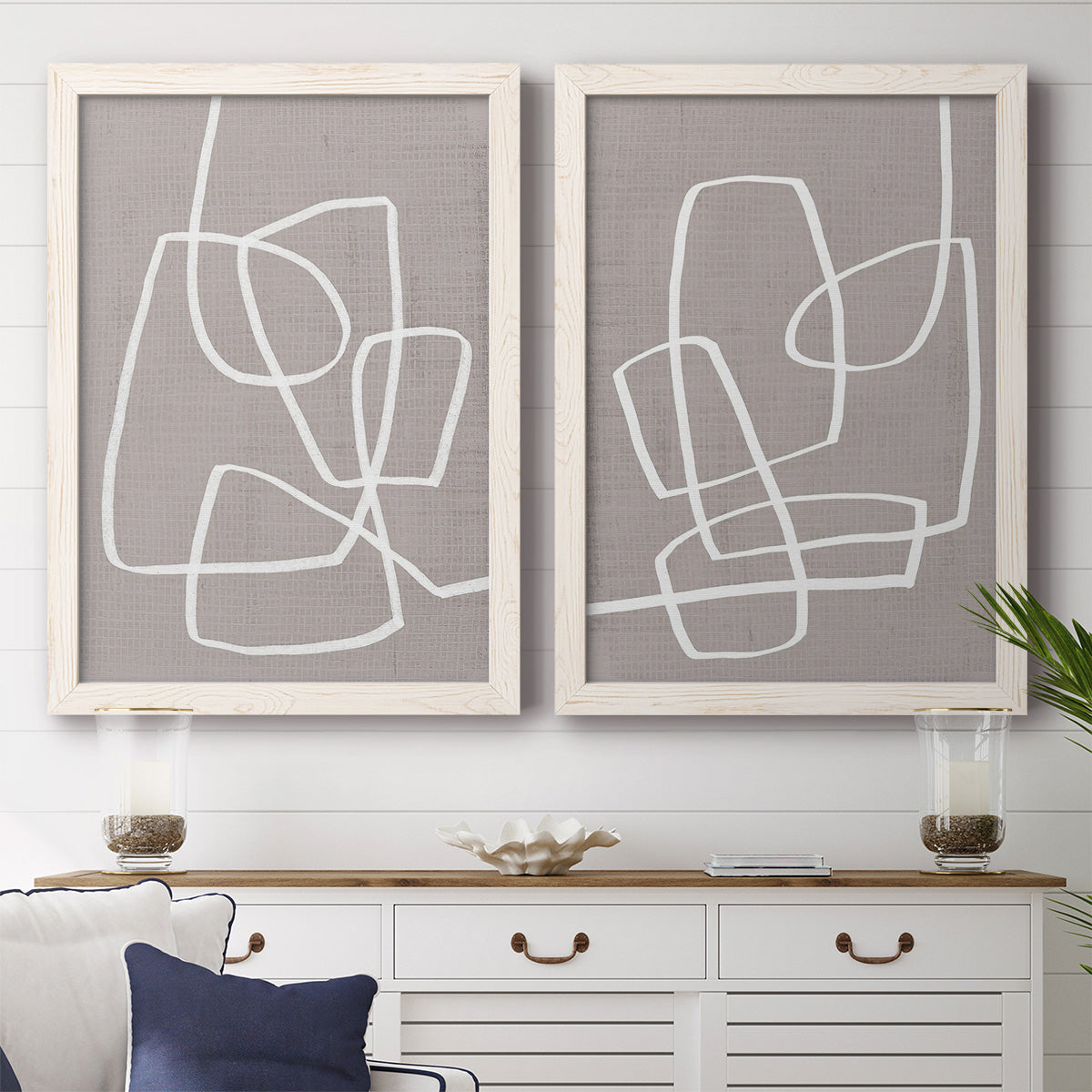 Set of two white barnwood framed canvas prints depicting a coordinated art pair of overlapping white continuous-line loops on taupe rendered as minimalist geometric line art above a dining room sideboard.