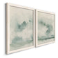 Angled view of a set of two white barnwood framed canvas prints featuring two minimalist watercolor seascapes with misty green clouds calm horizons and pale reflective water.
