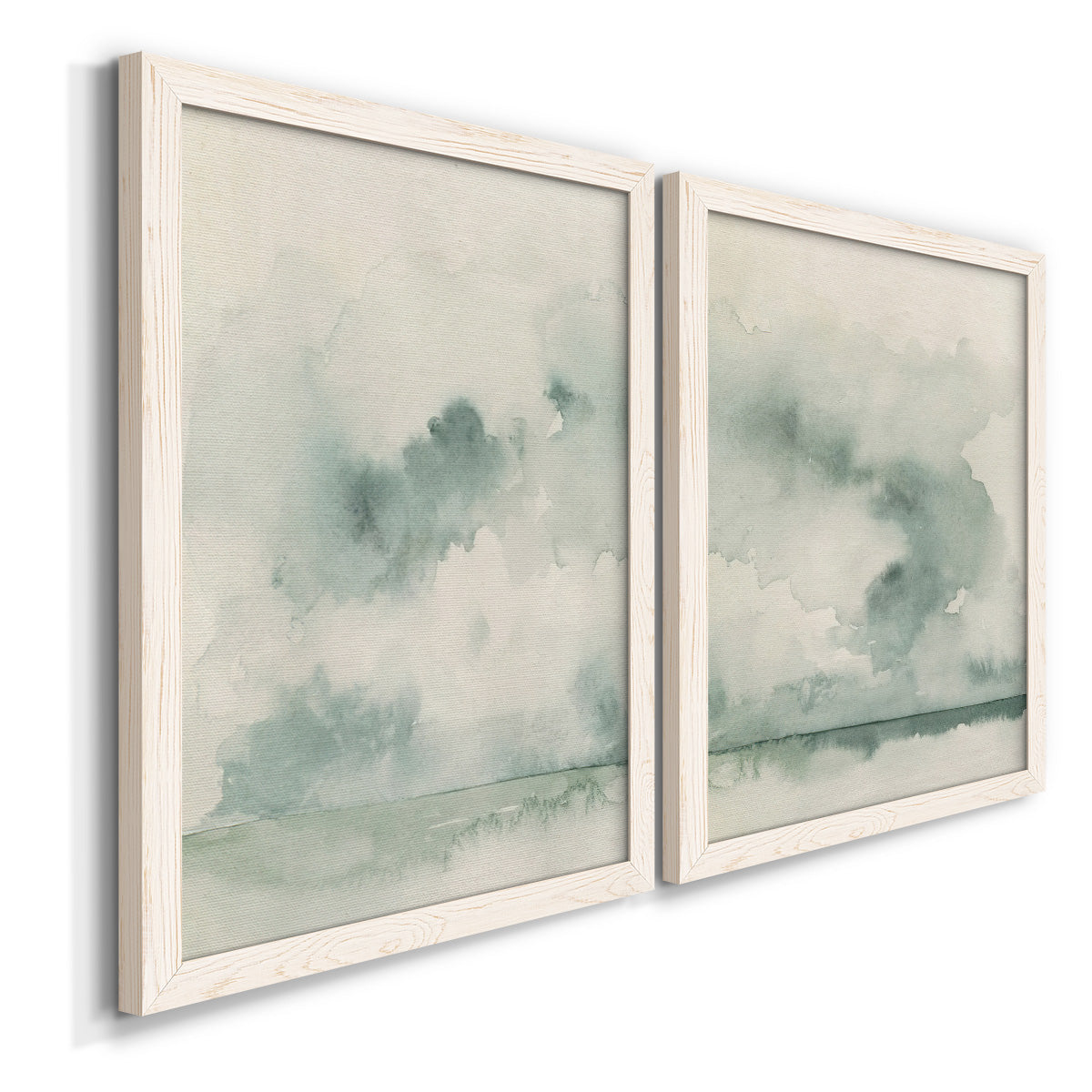 Angled view of a set of two white barnwood framed canvas prints featuring two minimalist watercolor seascapes with misty green clouds calm horizons and pale reflective water.