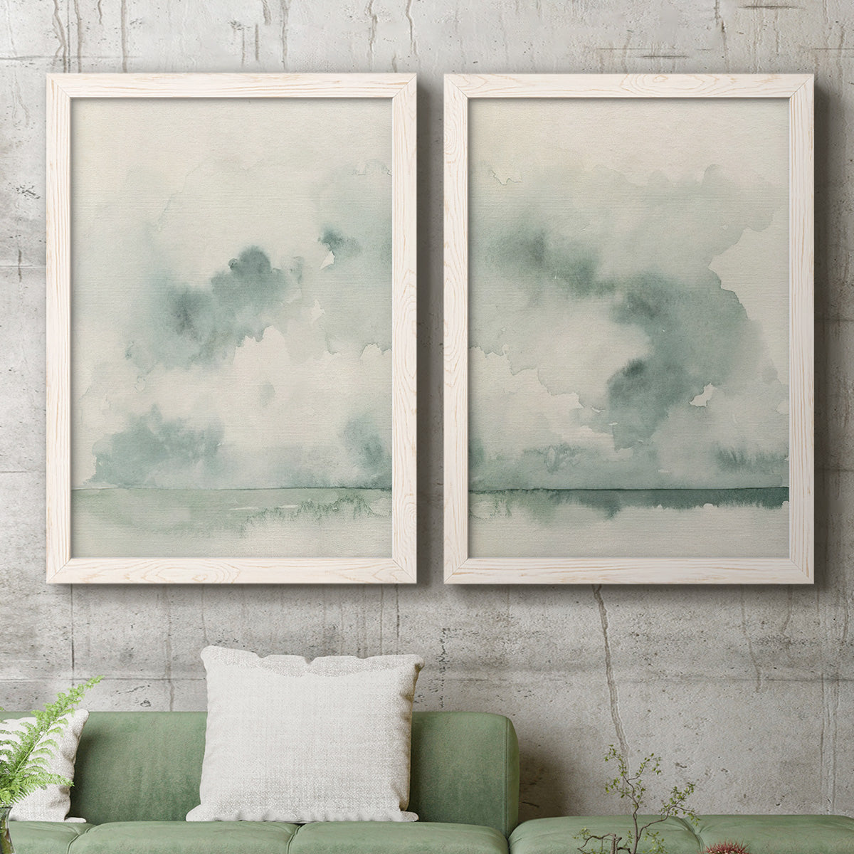 Set of two white barnwood framed canvas prints depicting a serene coastal pair of hazy skies distant shorelines and soft sage green washes above a sofa in a modern living room.