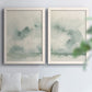 Set of two white barnwood framed canvas prints depicting abstract ocean horizons rendered in translucent gray green watercolor and quiet atmospheric layers above a sofa in a bright living space.
