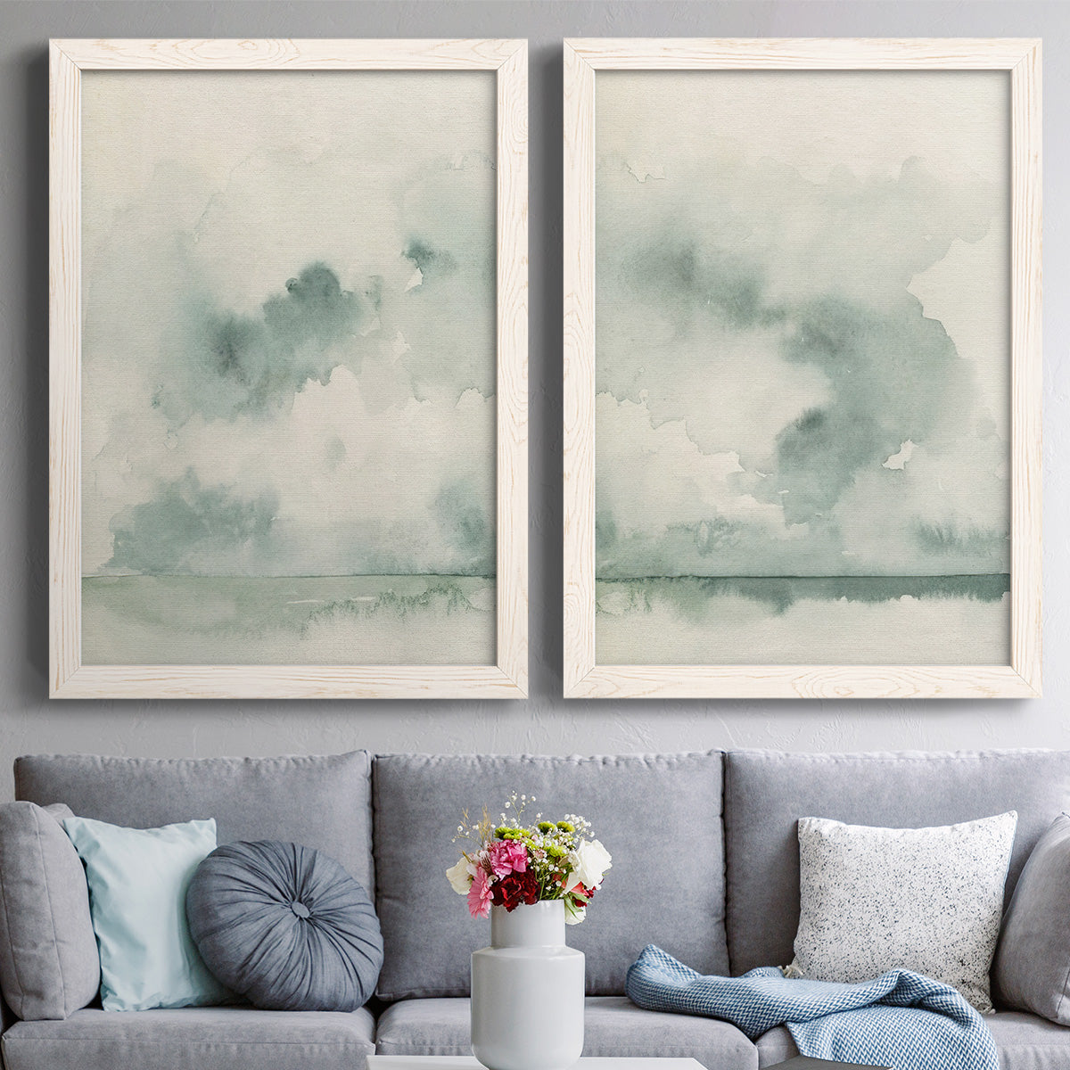 Set of two white barnwood framed canvas prints depicting soft coastal landscapes with cloudlike brushwork still water and a muted foggy palette above a sofa in a contemporary living room.