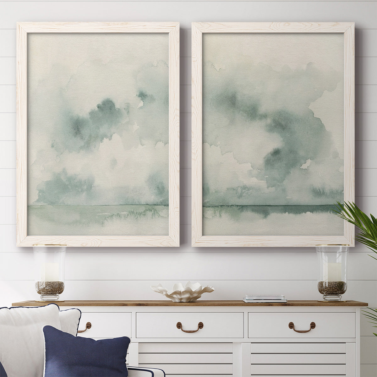 Set of two white barnwood framed canvas prints depicting a serene coastal pair of hazy skies distant shorelines and soft sage green washes above a dining room sideboard.