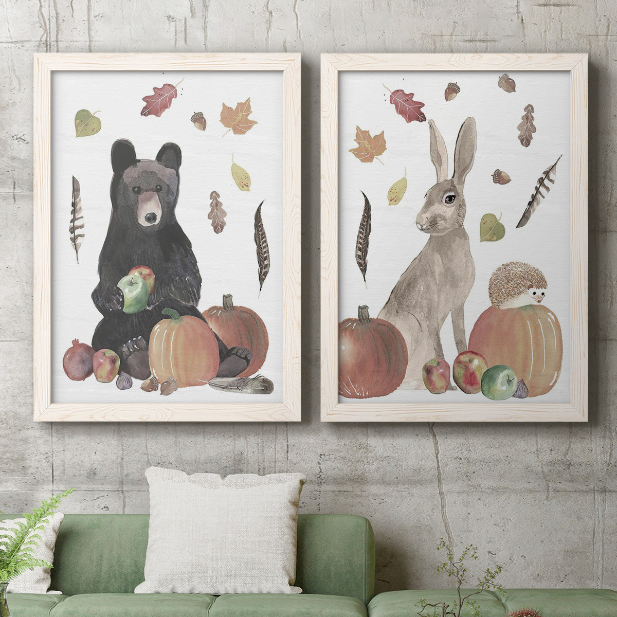 Set of two white barnwood framed canvas prints depicting two whimsical autumn illustrations of forest animals gathered among pumpkins apples feathers and seasonal foliage above a sofa in a modern living room.