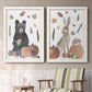 Set of two white barnwood framed canvas prints depicting a watercolor woodland animal pair with a bear rabbit hedgehog pumpkins fruit acorns and falling leaves above a sideboard in a cozy sitting room.