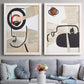 Set of two white barnwood framed canvas prints depicting paired mixed-media portrait collages with black contour features, red blocks, typography, and torn-paper textures above a sofa in a contemporary living room.