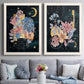 Set of two white barnwood framed canvas prints depicting paired whimsical floral collages with moons stars hanging jewels colorful blossoms and hand-lettered phrases above a sofa in a contemporary living room.