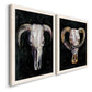 Angled view of a set of two white barnwood framed canvas prints featuring two dramatic Western animal paintings featuring ram and cattle skulls against black grounds.