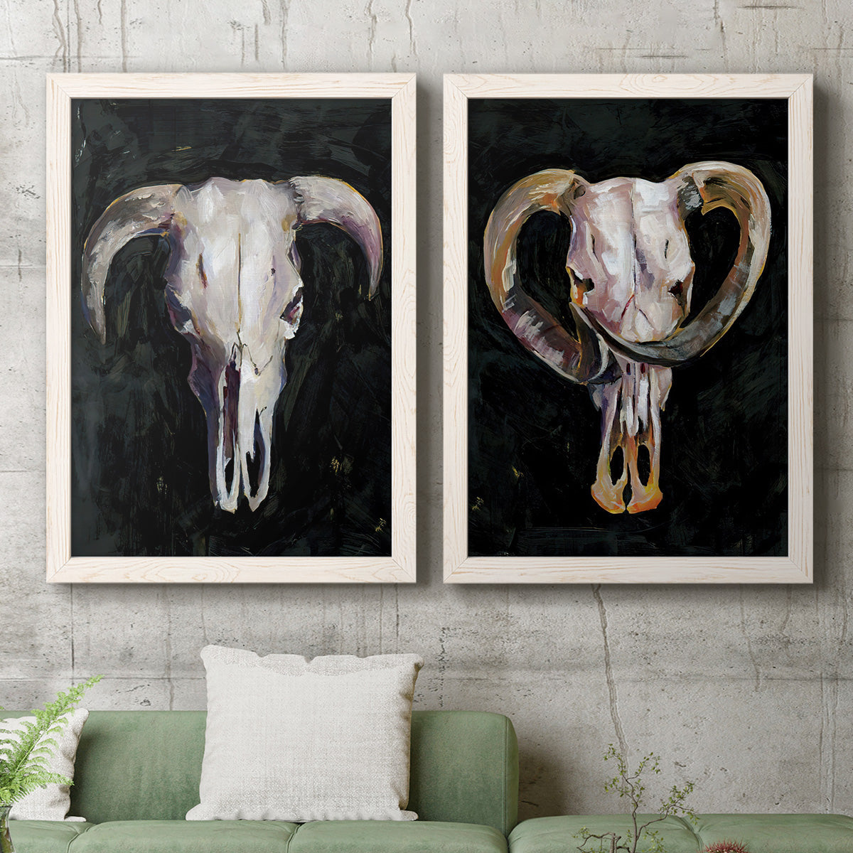 Set of two white barnwood framed canvas prints depicting a coordinated art pair of ram and cattle skulls against black grounds rendered as dramatic Western animal paintings above a sofa in a modern living room.