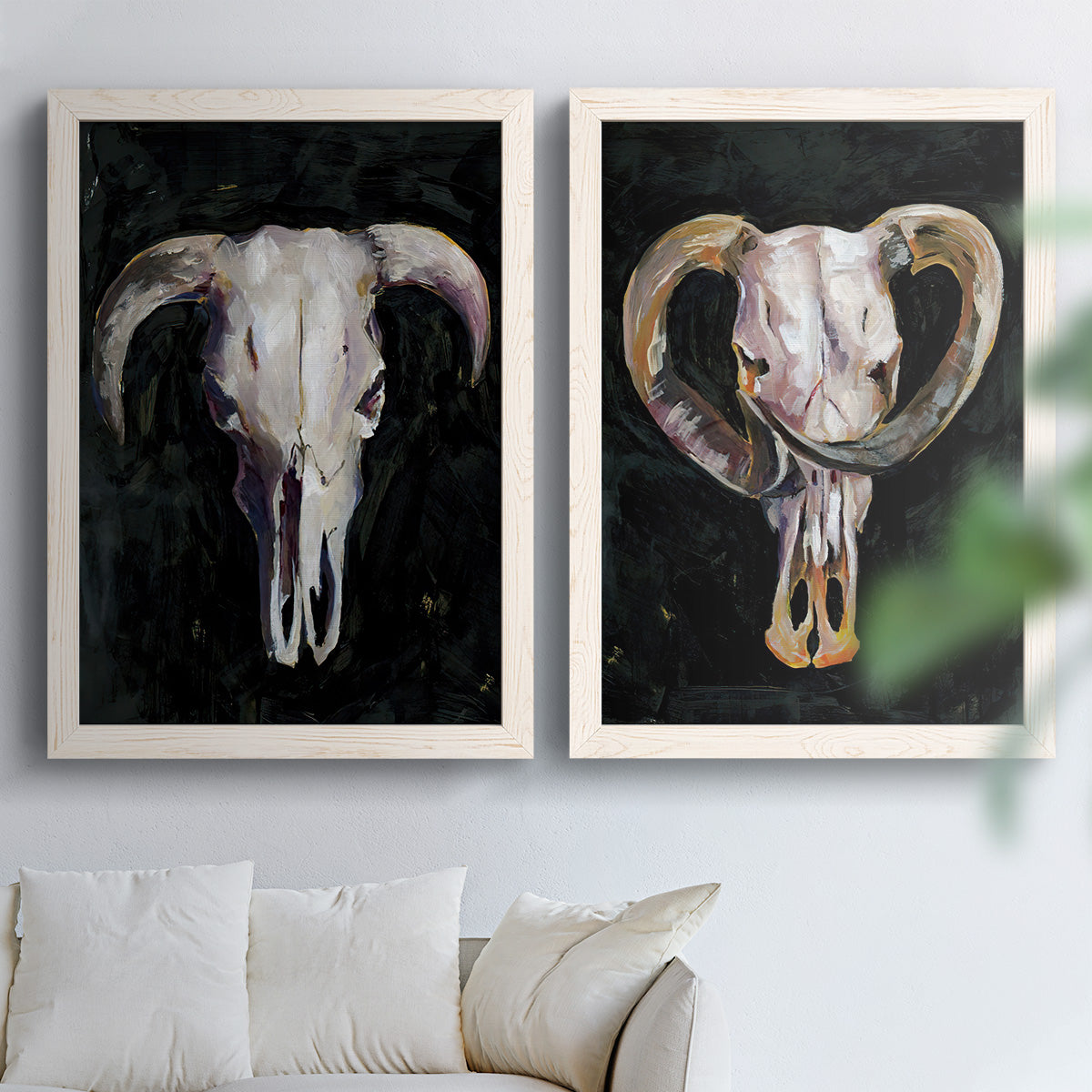 Set of two white barnwood framed canvas prints depicting curved horns, bone-white forms, and expressive dark brushwork arranged across two complementary compositions above a sofa in a bright living space.