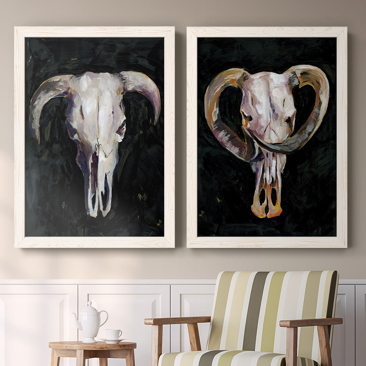 Set of two white barnwood framed canvas prints depicting two dramatic Western animal paintings featuring ram and cattle skulls against black grounds above a sideboard in a cozy sitting room.