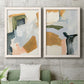 Set of two white barnwood framed canvas prints depicting a coordinated art pair of layered green ochre blush gray and white paint blocks rendered as contemporary mixed-media abstracts above a sofa in a modern living room.
