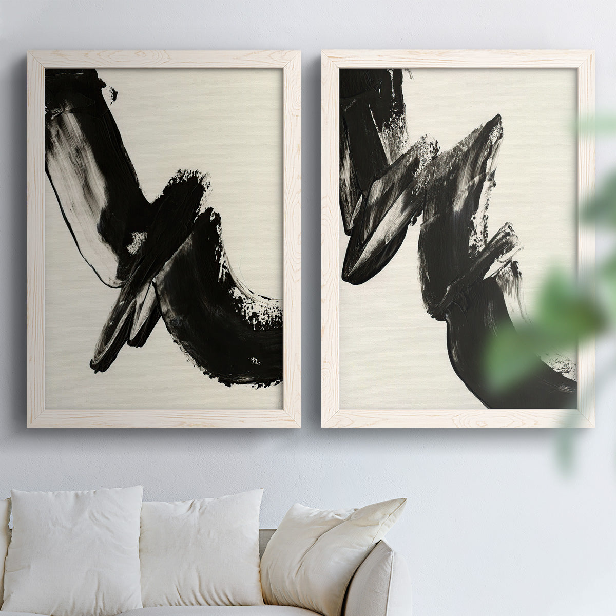 Set of two white barnwood framed canvas prints depicting thick ink-like marks, feathered edges, and cream negative space arranged across two complementary compositions above a sofa in a bright living space.