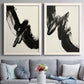 Set of two white barnwood framed canvas prints depicting paired bold gestural abstracts with thick ink-like marks, feathered edges, and cream negative space above a sofa in a contemporary living room.
