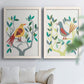 Set of two white barnwood framed canvas prints depicting red yellow blue plumage, simplified leaves, and playful flat shapes arranged across two complementary compositions above a sofa in a bright living space.