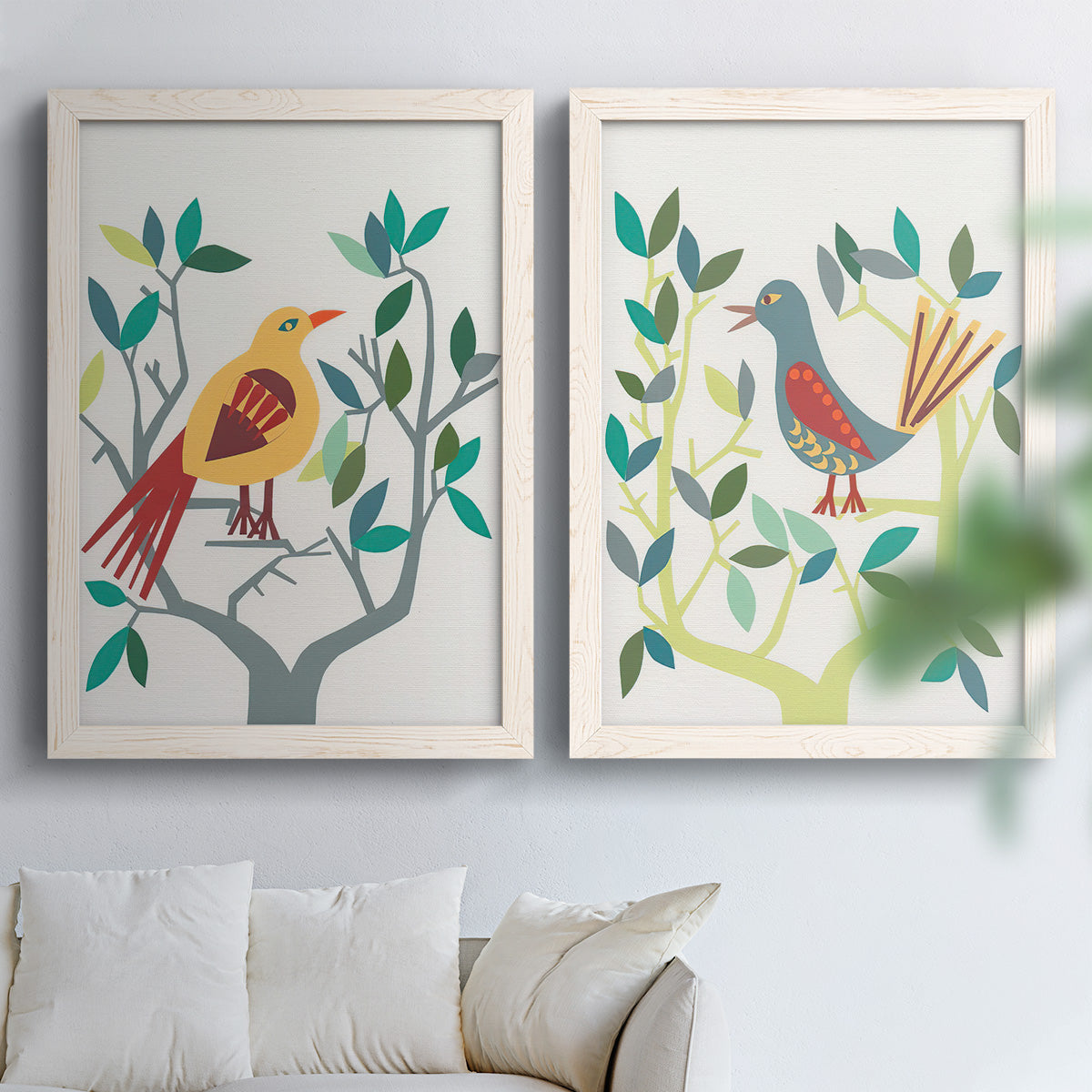 Set of two white barnwood framed canvas prints depicting red yellow blue plumage, simplified leaves, and playful flat shapes arranged across two complementary compositions above a sofa in a bright living space.