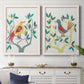 Set of two white barnwood framed canvas prints depicting a coordinated art pair of stylized colorful birds perched among leafy branches rendered as modern folk-art bird illustrations above a dining room sideboard.