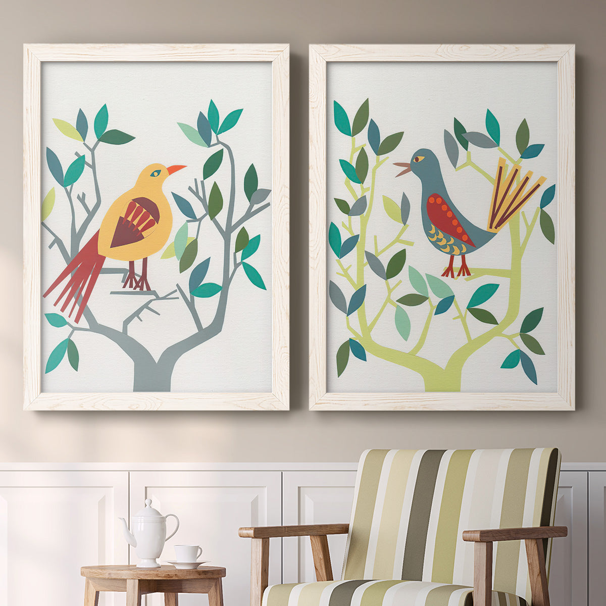 Set of two white barnwood framed canvas prints depicting two modern folk-art bird illustrations featuring stylized colorful birds perched among leafy branches above a sideboard in a cozy sitting room.