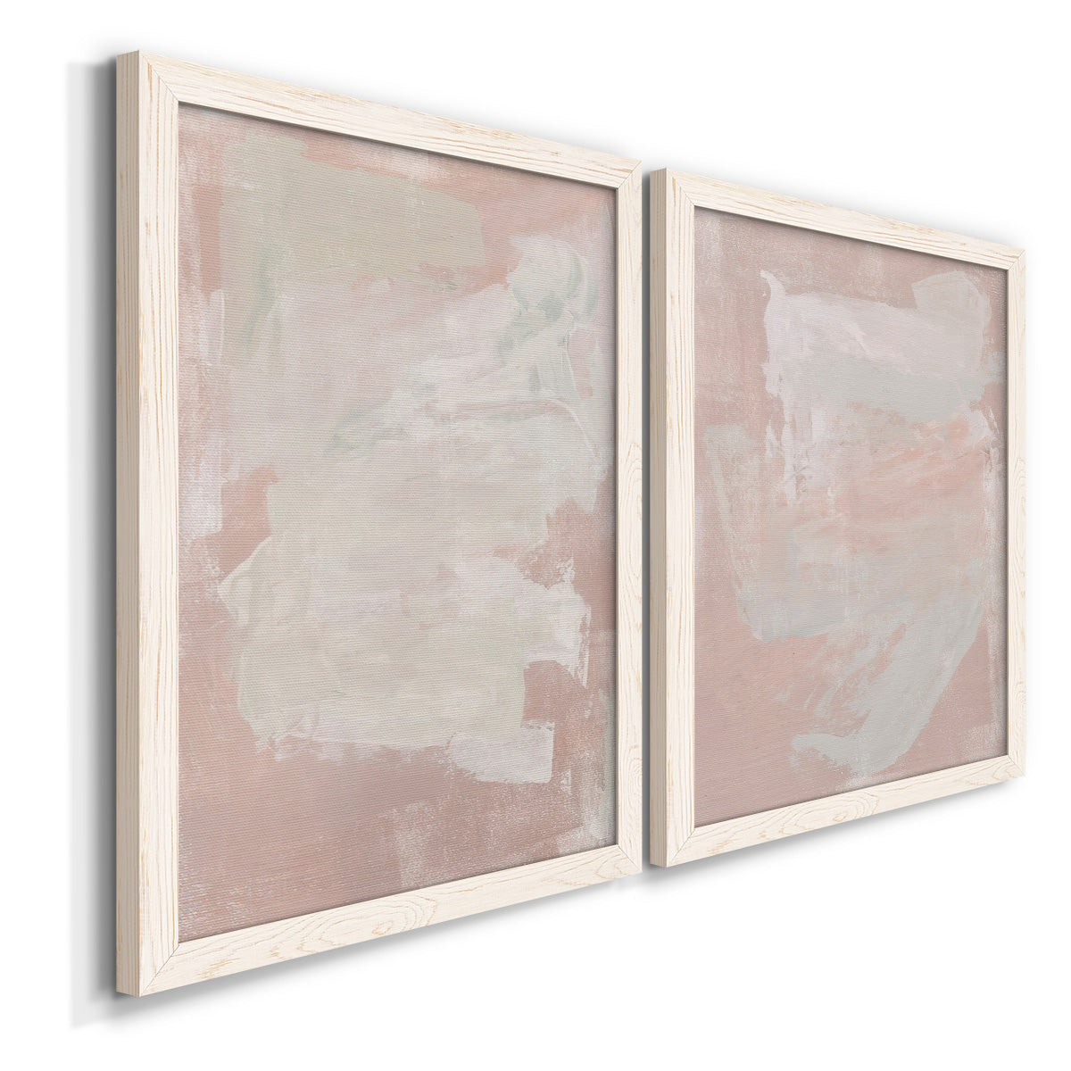 Angled view of a set of two white barnwood framed canvas prints featuring two minimalist color-field abstracts featuring soft blush and white painterly fields.