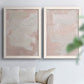 Set of two white barnwood framed canvas prints depicting cloudy rose washes, broad pale strokes, and subtle texture arranged across two complementary compositions above a sofa in a bright living space.