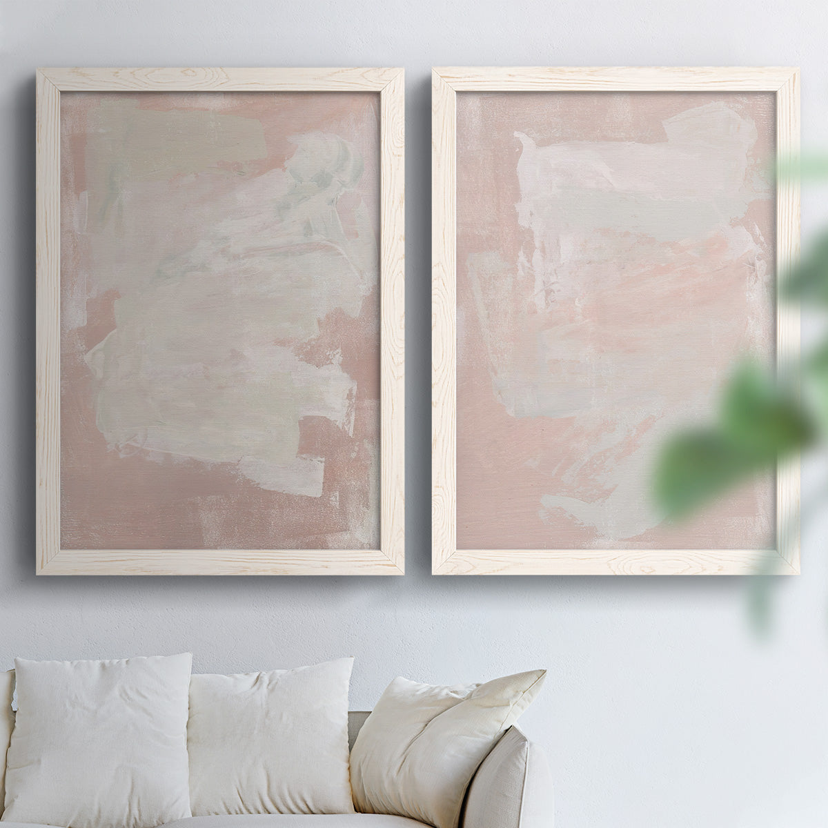 Set of two white barnwood framed canvas prints depicting cloudy rose washes, broad pale strokes, and subtle texture arranged across two complementary compositions above a sofa in a bright living space.