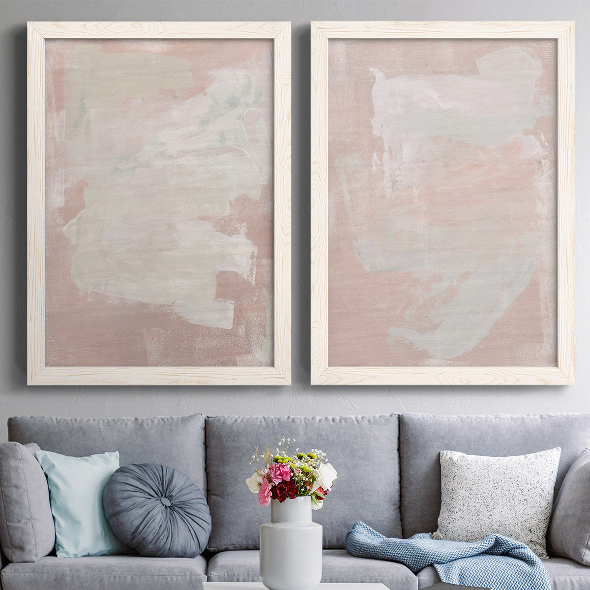 Set of two white barnwood framed canvas prints depicting paired minimalist color-field abstracts with cloudy rose washes, broad pale strokes, and subtle texture above a sofa in a contemporary living room.