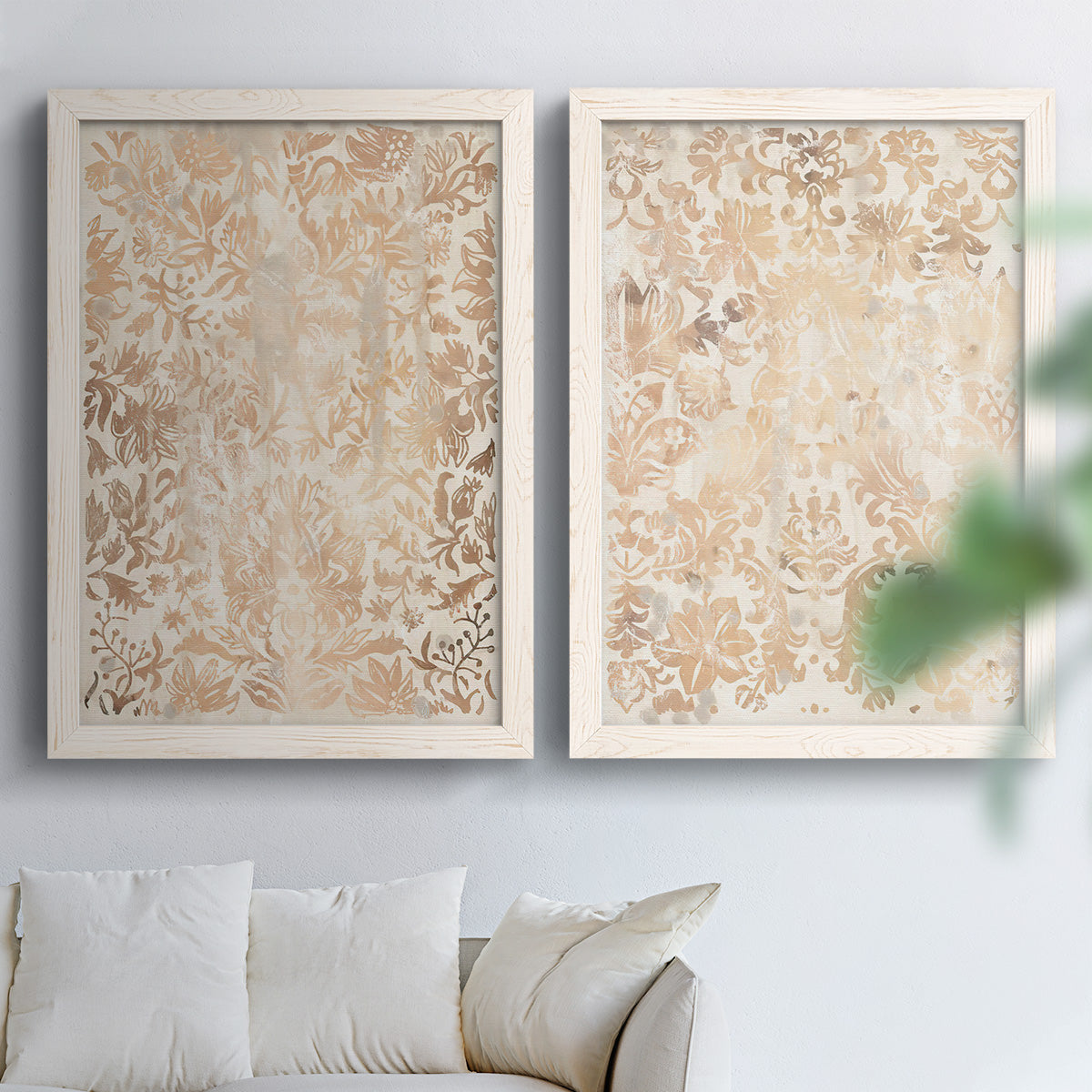 Set of two white barnwood framed canvas prints depicting dense scrolling foliage, distressed walnut-brown texture, and symmetrical motifs arranged across two complementary compositions above a sofa in a bright living space.