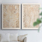 Set of two white barnwood framed canvas prints depicting dense scrolling foliage, distressed walnut-brown texture, and symmetrical motifs arranged across two complementary compositions above a sofa in a bright living space.